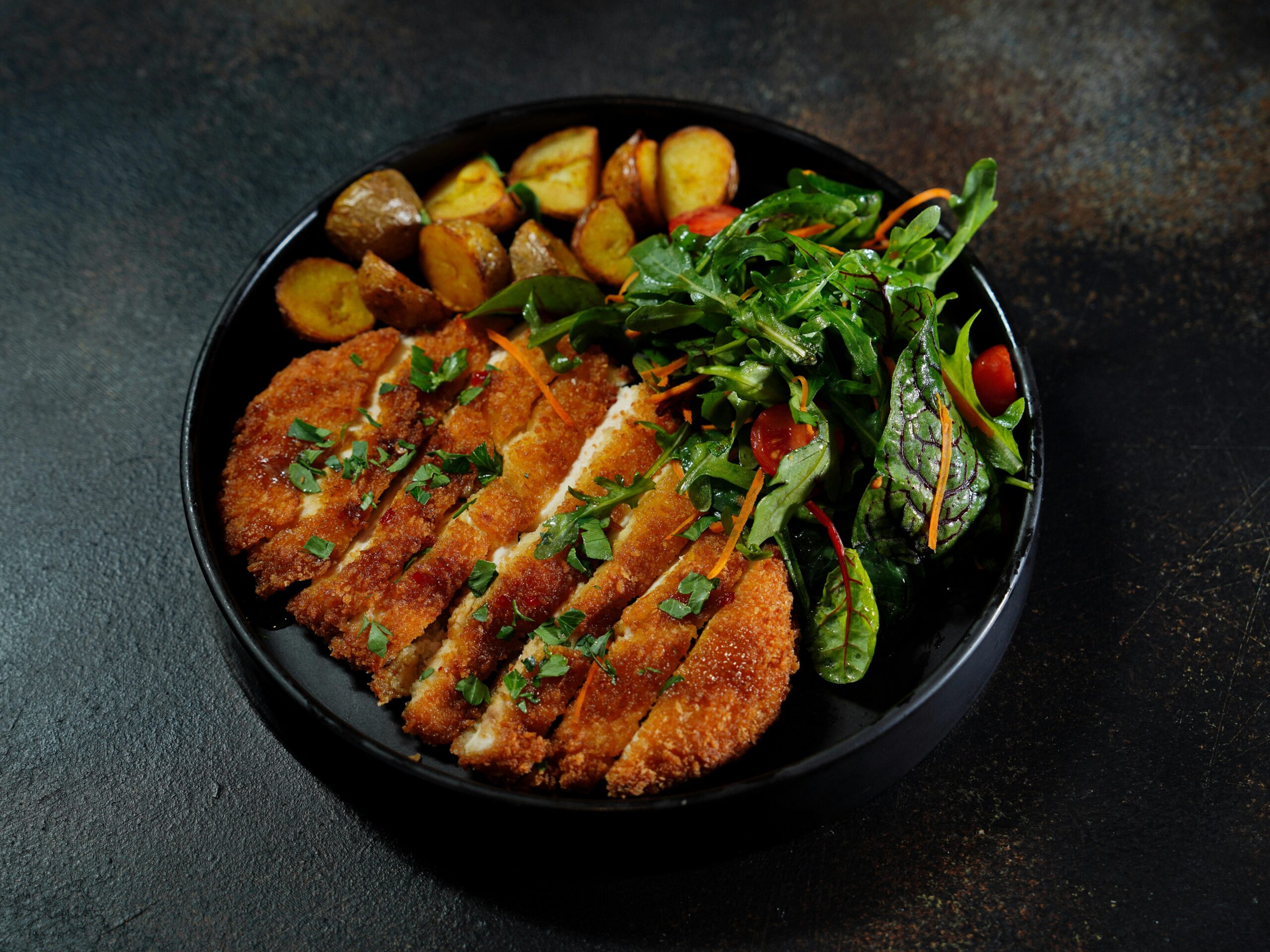 Delicious schnitzel served with roasted potatoes and fresh arugula salad.