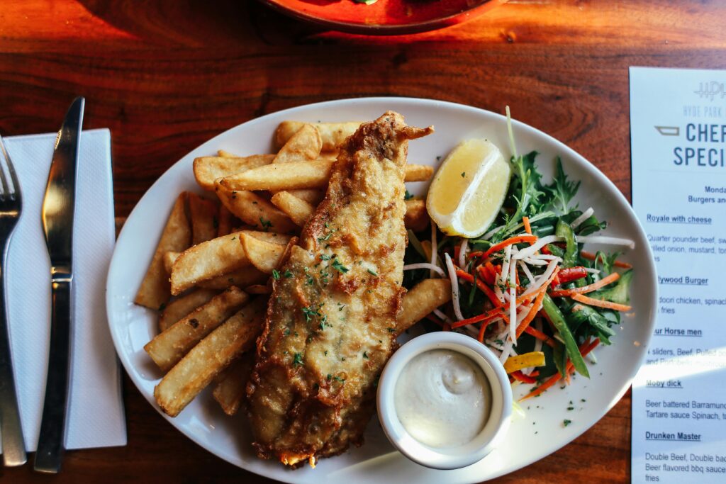 pexels-photo-5863643-5863643 Top view of crispy fish and chips with fresh salad and tartar sauce on a wooden table.